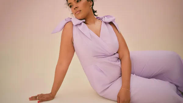 A woman in a lavender jumpsuit sits on one hip staring into the distance