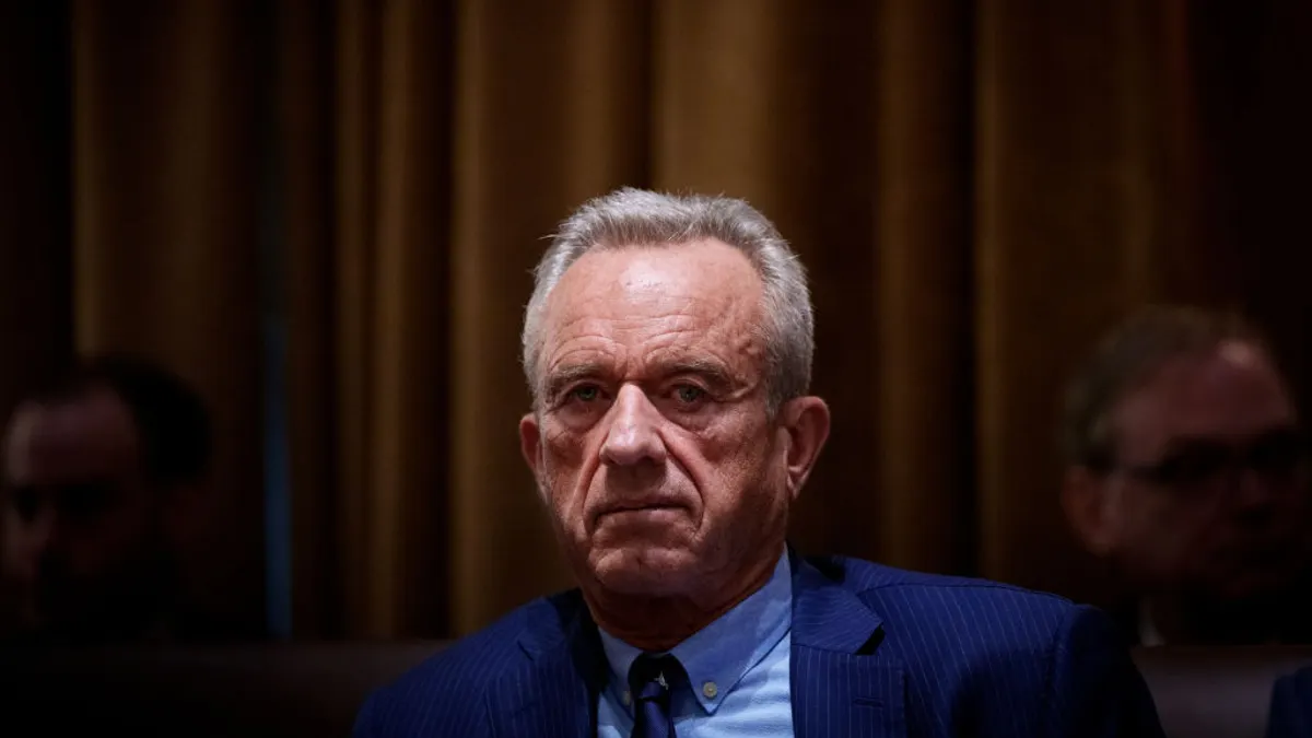 A person in a blue pinstripe suit looks straight ahead.