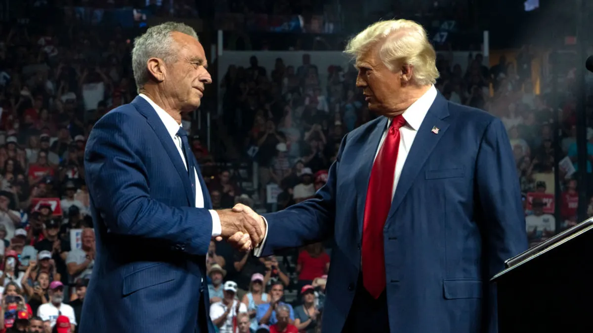 RFK Jr. shakes hands with Donald trump on stage with a crowd behind watching