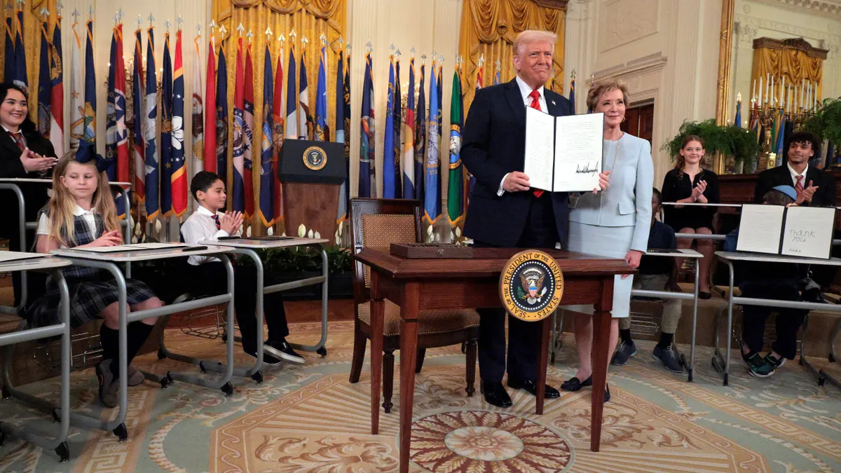 President Donald Trump stands next to Linda McMahon while holding the executive order in the White House.