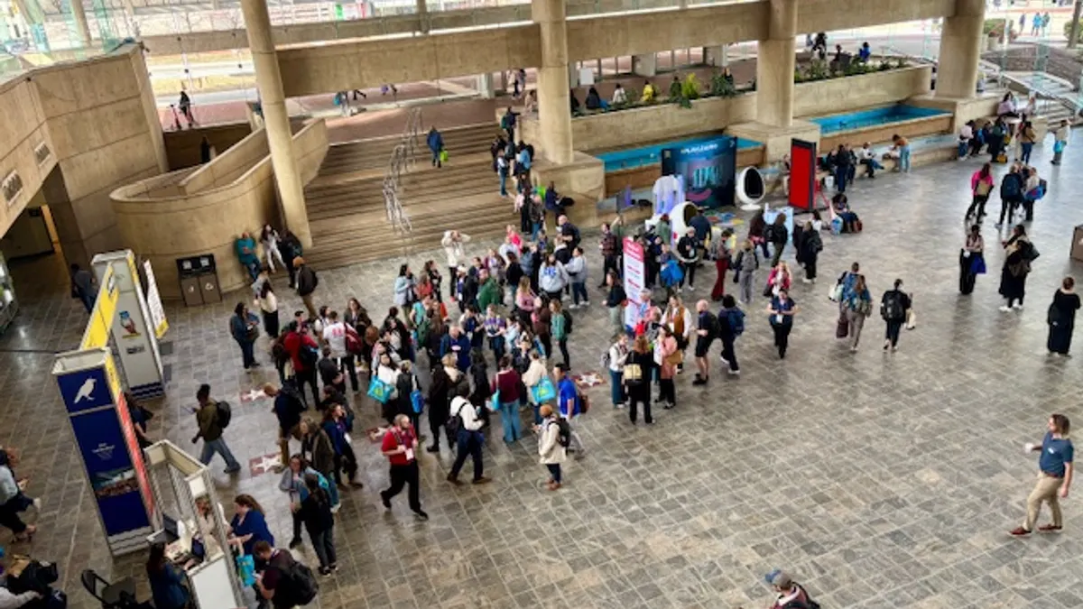 A crowd of people are standing in a lobby of a convention center. They are seen from an above angle.